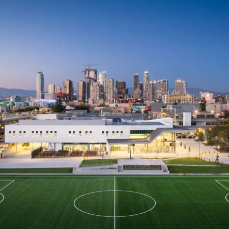 Los Angeles Trade Tech College. Wide shot of the dining building. Soccer field lies in front of the illuminated building, with the cityscape dotting the skyline behind.