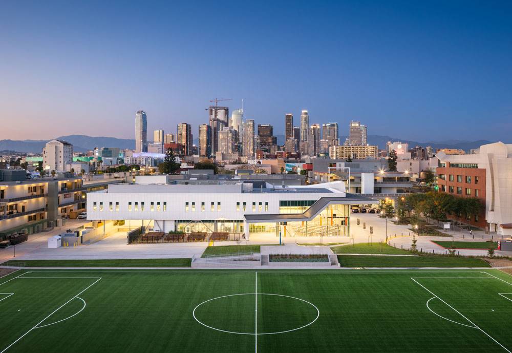 Los Angeles Trade Tech College. Wide shot of the dining building. Soccer field lies in front of the illuminated building, with the cityscape dotting the skyline behind.