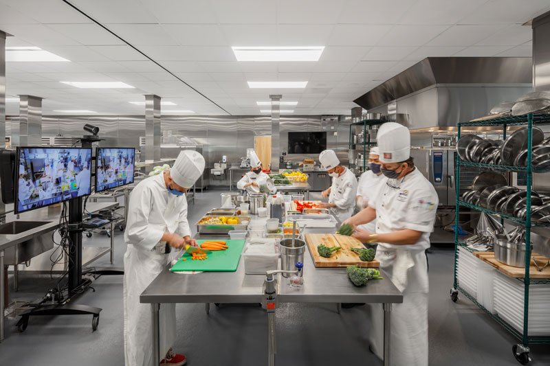 Los Angeles Trade Tech College. Commercial kitchen with five chefs chopping vegetables at the kitchen island.