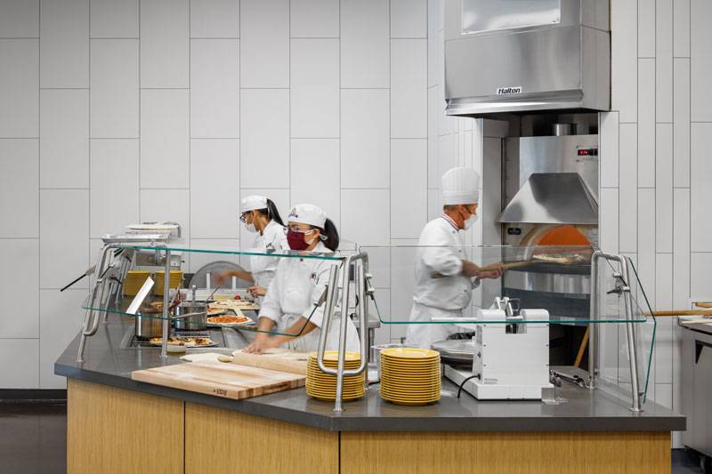 Los Angeles Trade Tech College. Three chefs work behind a counter making pizza.