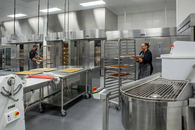 Sacramento City Unified School District. Chefs in Central Kitchen stack trays onto tray rack.