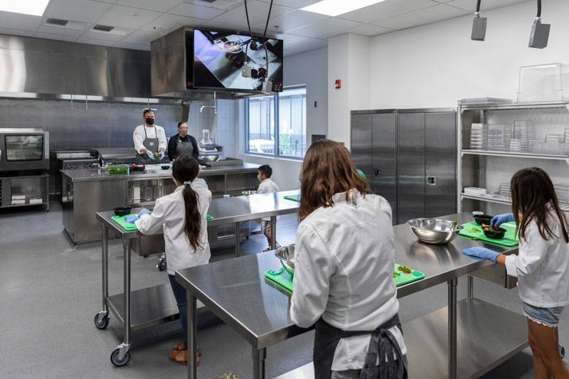 Sacramento City Unified School District. Young chef proteges practice cooking at Central Kitchen islands guided by two head chefs.